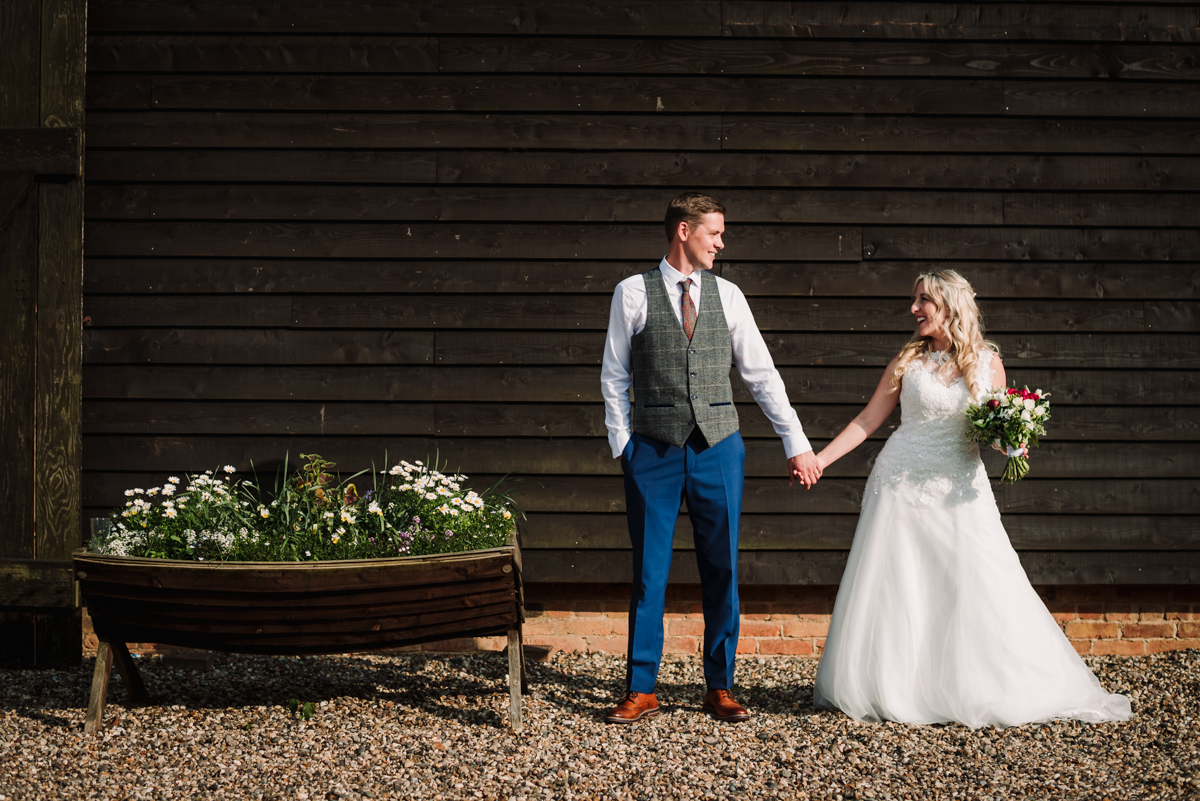 Bride and groom hold hands in the sun in front of Rowley Barn