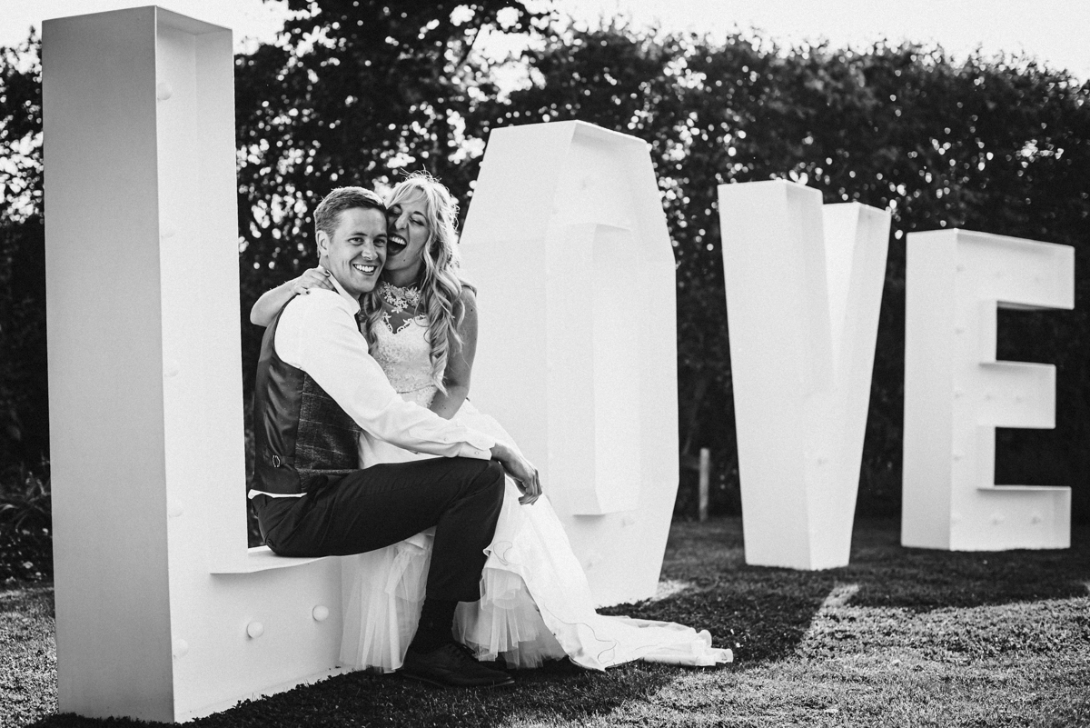 Bride and groom sit on love letters in the gardens of Rowley Barn in Hertfordshire