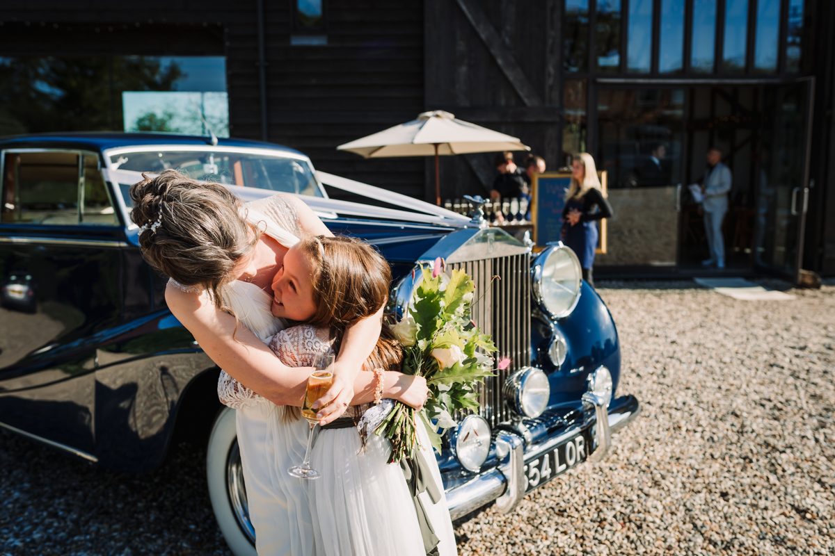Bride cuddles her little bridesmaid on arrival to Rowley Barn