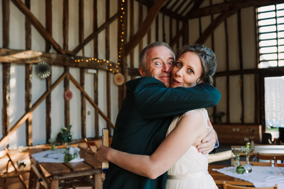 Bride pulls a funny face at the wedding photographer as she hugs a guest
