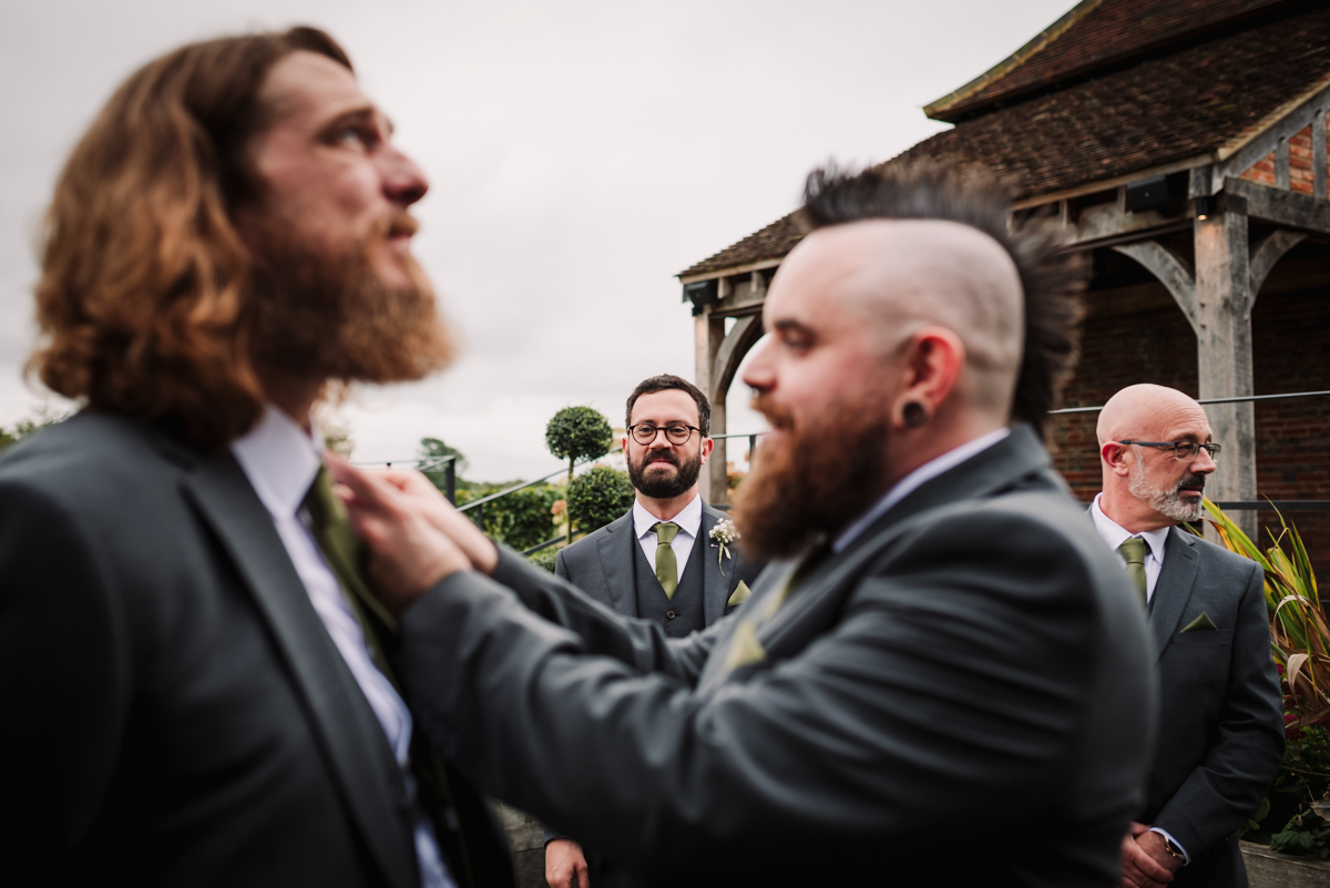 Groomsmen struggle to put on their buttonholes at The Farmhouse at Redcoats