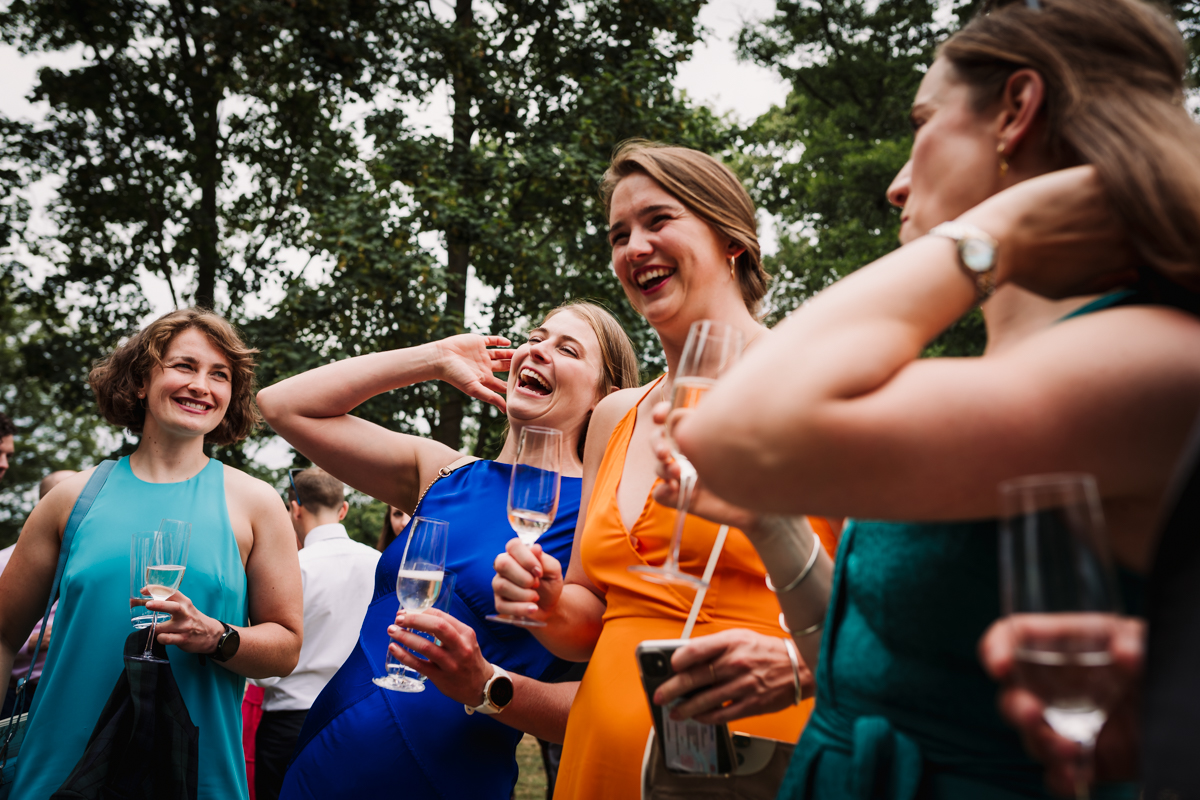 Laughing wedding guests enjoy champagne on arrival to festival wedding