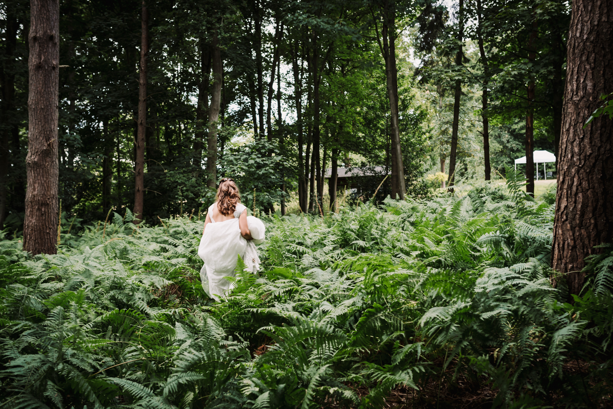 Brides walks through the woods at her family home which hosts her summer festival wedding