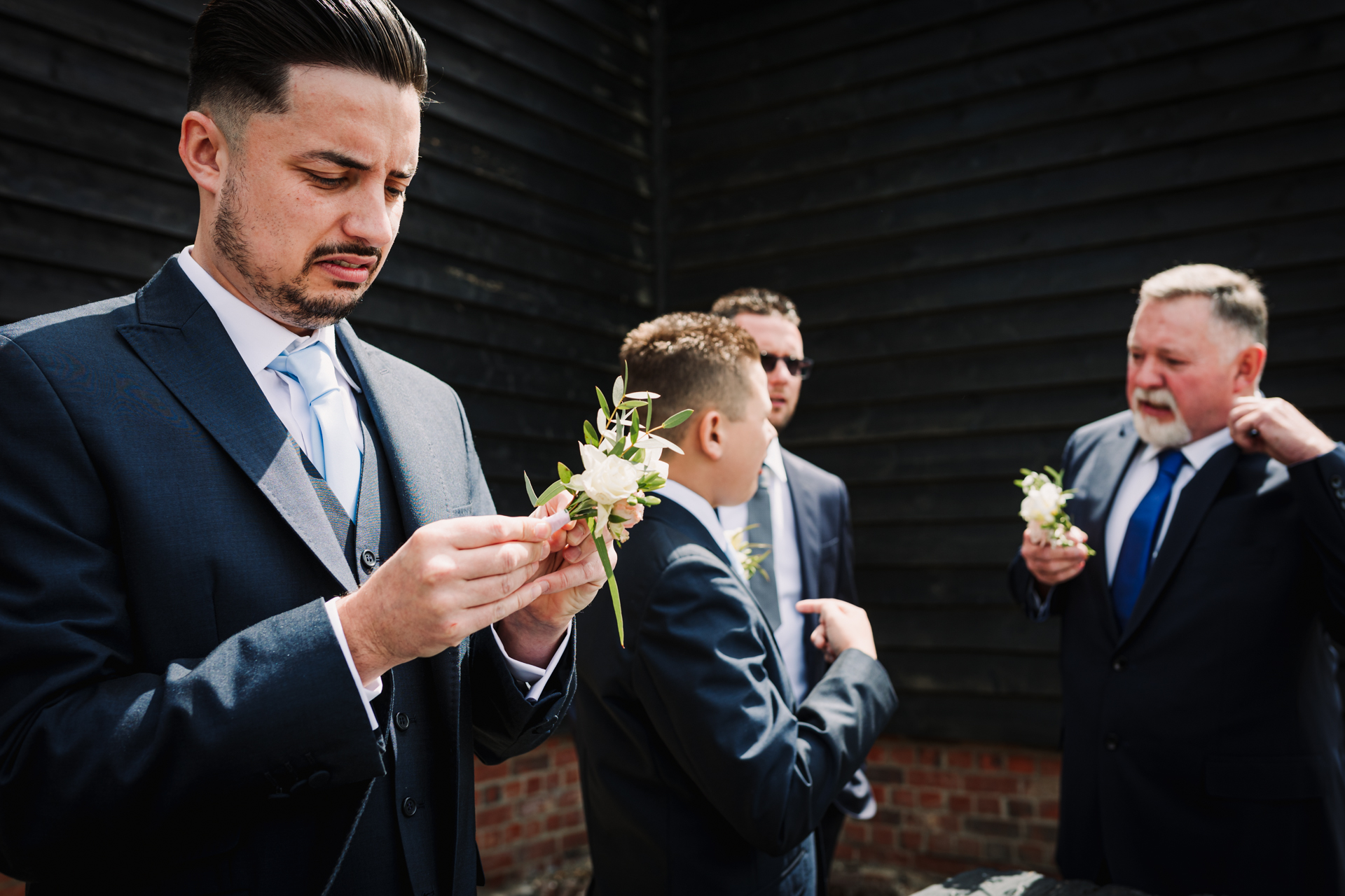 Groomsman looks confused as he tries to put on his wedding button hole