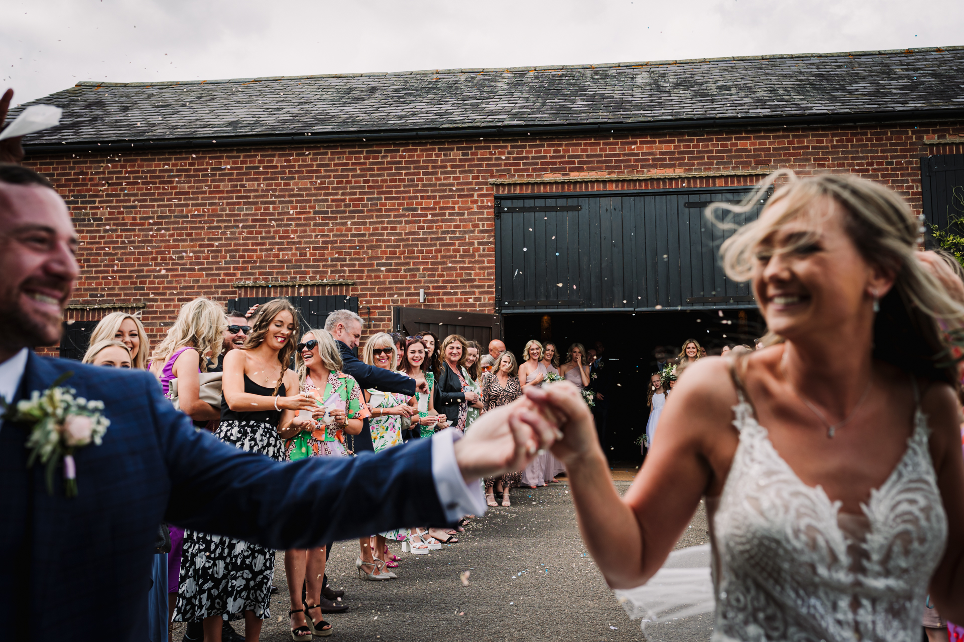 Guests throw confetti stood out side the oak barn at Milling Barn