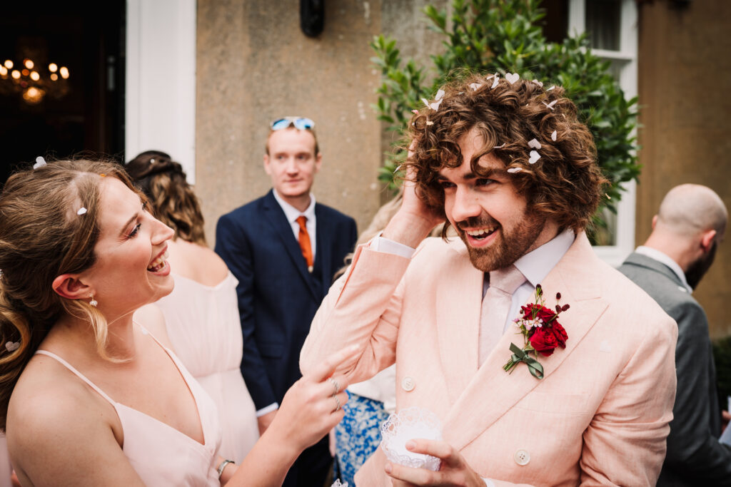 best man gets help from a bridesmaid as his hair is full of confetti